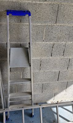 une échelle appuyée contre un mur de briques, avec une chaise posée dessus