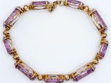 a close up of a purple and gold bracelet on a white surface