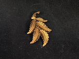 a close up of a gold leaf brooch on a black cloth