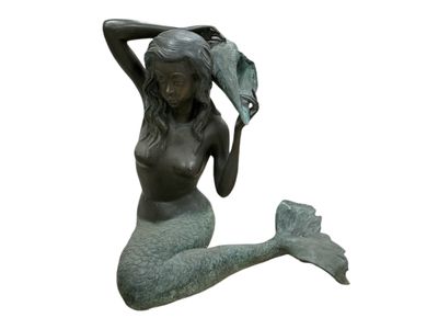une statue représentant une sirène assise par terre, les mains sur la tête