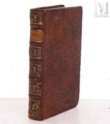 un vieux livre marron aux tranches dorées posé sur une table blanche