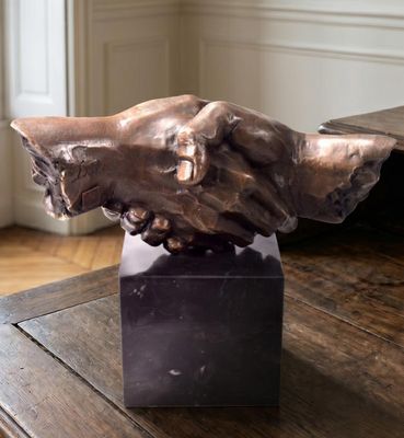 a bronze sculpture of a handshake on top of a wooden table