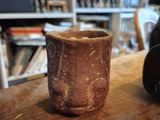 a brown cup sitting on a wooden table in front of a bookshelf