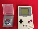 an old gameboy with a game and a case on a red table