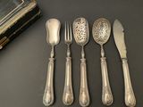six antique silverwares and a book sit on a table