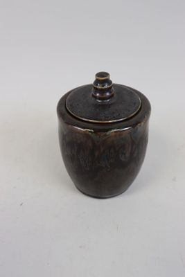 un petit bol marron avec un couvercle, posé sur une surface blanche