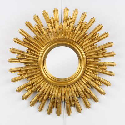 un miroir doré à rayons soleil accroché au mur, à côté d'un mur blanc