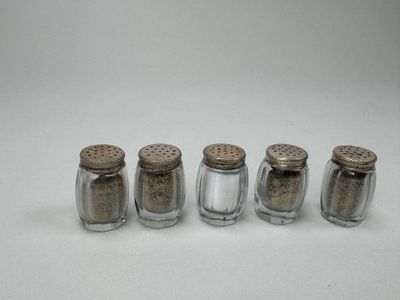 four glass salt shakers lined up in a row on a white surface