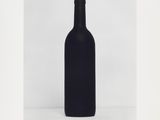 a black bottle of wine sitting on top of a white table