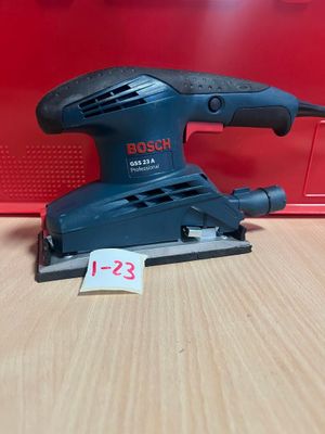 une ponceuse orbitale Bosch posée sur une table, à côté d'une boîte rouge