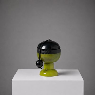 un vase noir et vert posé sur un socle blanc