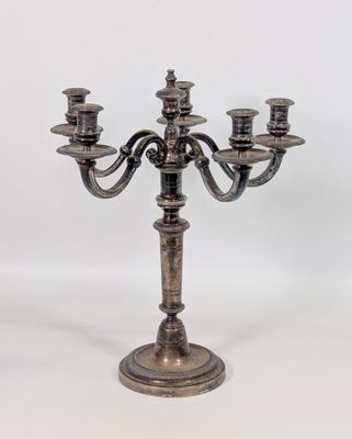 un candélabre ancien en métal argenté, à cinq bougies, posé sur un socle