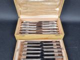 une photo d'un ensemble de six couteaux en métal argenté dans un coffret en bois
