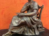 une statue en bronze d'une femme assise sur une chaise à côté d'une horloge