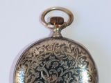 une montre de poche en argent posée sur une surface blanche