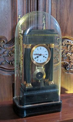 a clock that is under a glass cover on a shelf