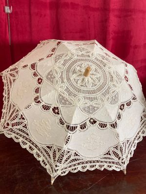 un parapluie en dentelle blanche posé sur une table à côté d'un rideau rouge