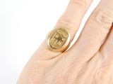 a woman ' s hand holding a gold ring with a crest on it