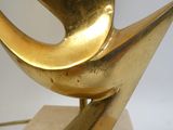 une sculpture en or représentant un oiseau, posée sur un socle en marbre