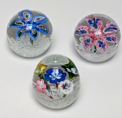 trois presse-papiers en verre ornés de fleurs, posés sur une surface blanche