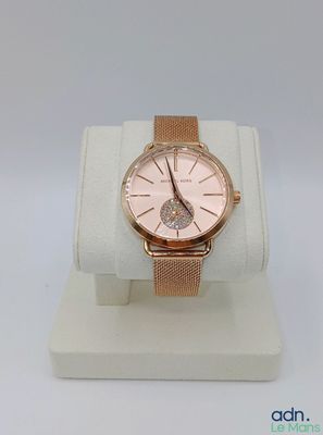 La montre est exposée sur un présentoir blanc, avec un bracelet rose.