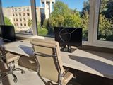 a desk with two computers and a chair in front of a large window
