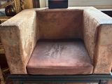 fauteuil en velours marron placé devant une fenêtre, dans une pièce au sol en briques rouges