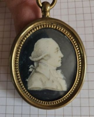 une petite image représentant un homme coiffé d'un chapeau, suspendu à une chaîne