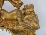 a gold statue of a man laying on a bed with a clock