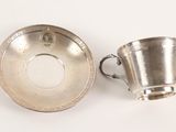 silver cup and saucer on a white surface with a coin in the background