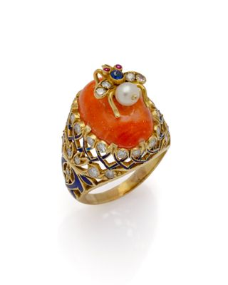 un gros plan d'une bague en or sertie d'une pierre orange et d'une perle