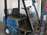 un chariot élévateur bleu garé dans un garage, à côté d'un mur blanc