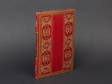 un vieux livre à la couverture rouge, rehaussée de dorures sur un fond gris