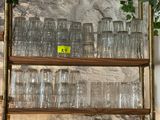bottles and glasses on a shelf in a room with a stone wall