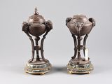 pair of bronze vases with handles on stands on a gray surface