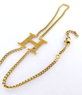 a close up of a gold chain bracelet with a letter h on it