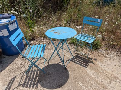 deux chaises et une table posées à même le sol, près d'une poubelle