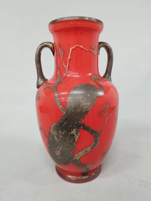 un vase rouge orné d'un oiseau perché sur une branche d'arbre