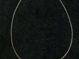 a gold chain necklace with a white pearl on a black background