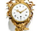 a gold clock on a white wall with a statue on top of it