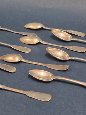 six cuillères en argent sont alignées les unes à côté des autres sur une surface bleue