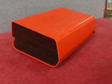 une enceinte orange posée sur un tapis rouge, près d'un mur
