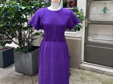 une robe violette posée sur un mannequin devant un immeuble