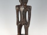 une statue en bois représentant un homme debout, les mains dans les poches