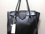 un sac à main en cuir noir accroché à un mur, avec une étiquette attachée dessus