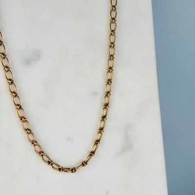 un gros plan d'un collier à chaîne en or posé sur une surface en marbre