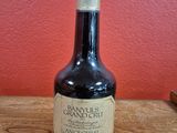 an old bottle of brandy sits on a wooden table in front of a red wall