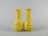 pair of yellow vases sitting on a white surface with a gray background