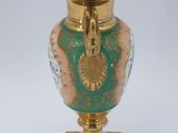 a green and gold vase on a gold stand