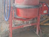 a red cement mixer sitting in front of a brick wall